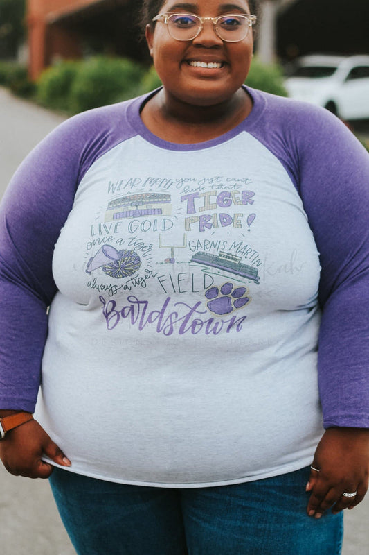 A person wearing a long-sleeved purple and white t-shirt with hand-drawn lettering and designs.