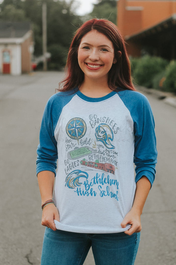 A person wearing a long-sleeved baseball tee with blue sleeves and white body, featuring hand-drawn lettering and designs related to Bethlehem High School.