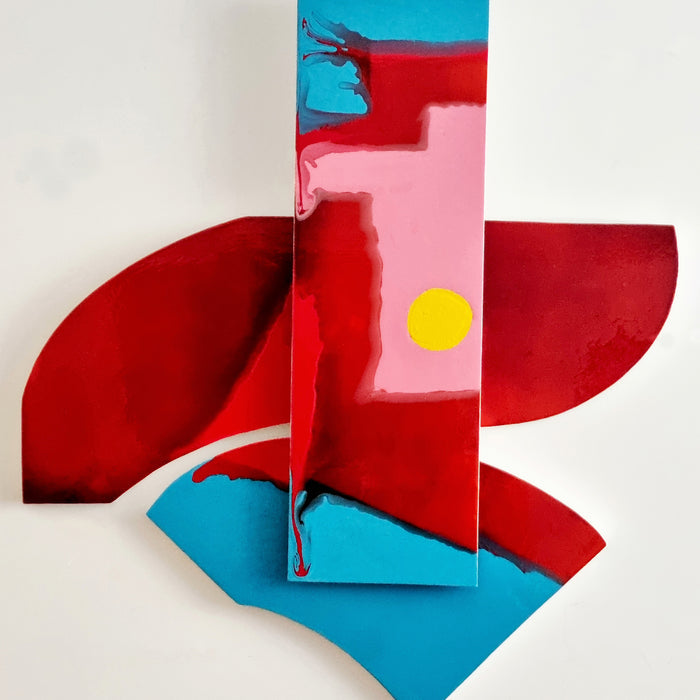 The artwork 'Is It Real or Am I Dreaming 5' by Sabrina Puppin features bold geometric shapes in vibrant red, turquoise blue, and soft pink, with a striking yellow circular accent. The composition combines curved and angular forms in a glossy synthetic glaze finish on wood, creating a dynamic abstract design with fluid color transitions.