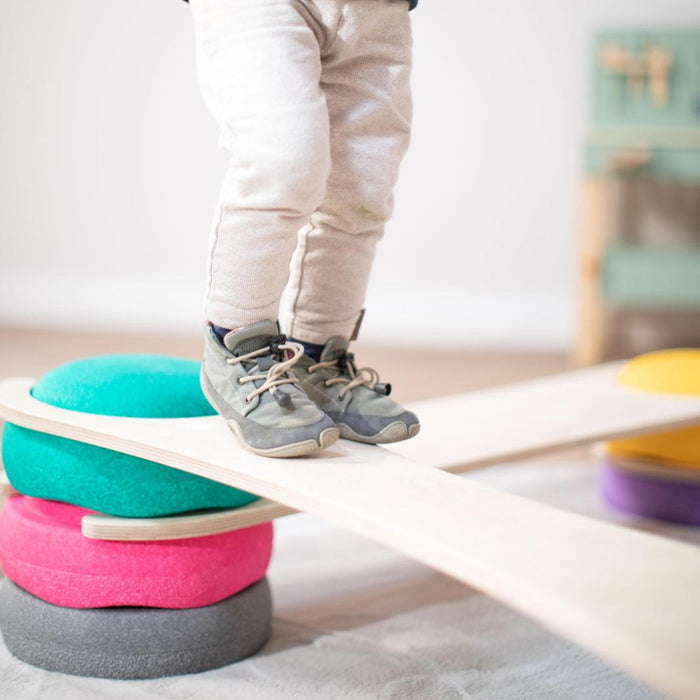 Kind balanciert auf dem tiSsi Balance Board mit Stapelsteinen zur Förderung von Gleichgewicht, Motorik und Bewegung im Alltag